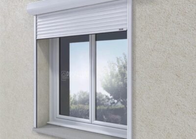 Volet roulant blanc semi-ouvert installé en applique sur une fenêtre à double vitrage, en façade extérieure crépie.