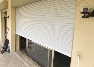 Volet roulant blanc en aluminium à moitié descendu devant une large baie vitrée, installé sur la façade d’un appartement.