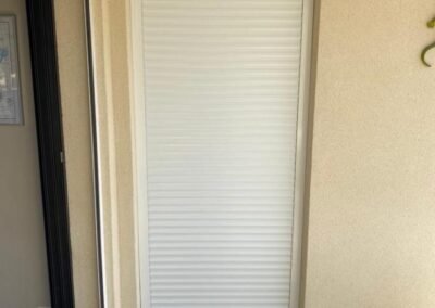 Volet roulant blanc fermé sur une porte-fenêtre extérieure, installé sur une façade beige avec sol carrelé.