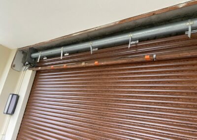 Vue rapprochée d’un volet roulant en métal imitation bois, avec son axe apparent dans un coffre mural partiellement ouvert.