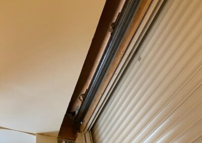 Vue en contre-plongée d’un volet roulant intérieur partiellement ouvert, montrant le coffrage en bois et les glissières métalliques latérales.